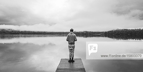 Junger Mann steht auf einem Steg und schaut über einen See  neblige Atmosphäre  Lake Mapourika  Westküste  Südinsel  Neuseeland  Ozeanien