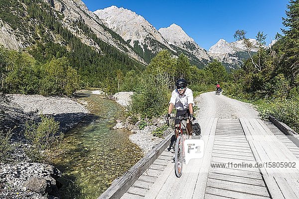 Cyclist  mountain biker bikes on bridge over mountain stream  gravel path to Karwendelhaus  Karwendel valley  Tyrol  Austria  Europe