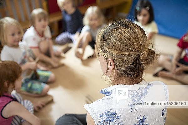 Erzieherin sitzt in einem Kindergarten mit Kindern im Kreis und macht Spiele  Köln  Nordrhein-Westfalen  Deutschland  Europa
