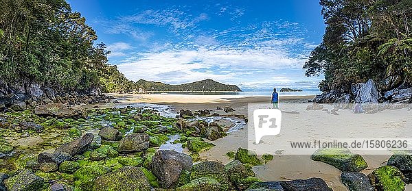 Junge Frau steht am Strand mit moosbewachsenen Felsen  Stillwell Bay  Bach Lesson Creek  Abel Tasman Coastal Track  Abel Tasman National Park  Tasman  Südinsel  Neuseeland  Ozeanien