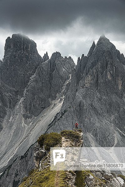 Man with red jacket standing on one degree  behind him mountain peaks and pointed rocks  dramatic clouds  Cimon the Croda Liscia and Cadini group  Auronzo di Cadore  Belluno  Italy  Europe