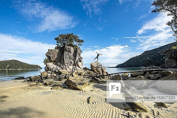 Young man standing with outstretched arms on a rock  overgrown rock on the beach of Stillwell Bay  Abel Tasman National Park  Tasman  South Island  New Zealand  Oceania