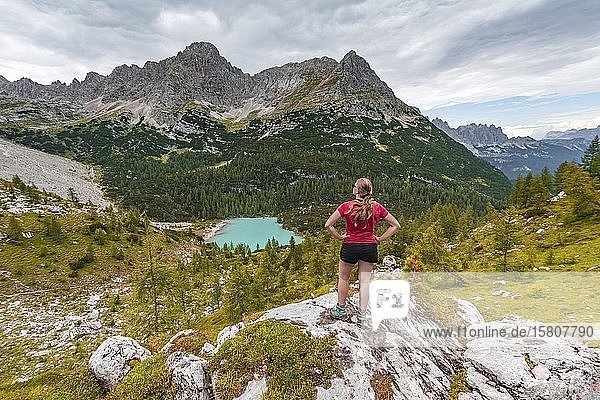 Young woman  hiker stands on rocks and looks at turquoise green Sorapiss lake and mountain landscape  Dolomites  Belluno  Italy  Europe