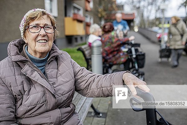 Seniorin sitzt auf einer Bank vor einer Seniorenwohnanlage  Köln  Nordrhein-Westfalen  Deutschland  Europa