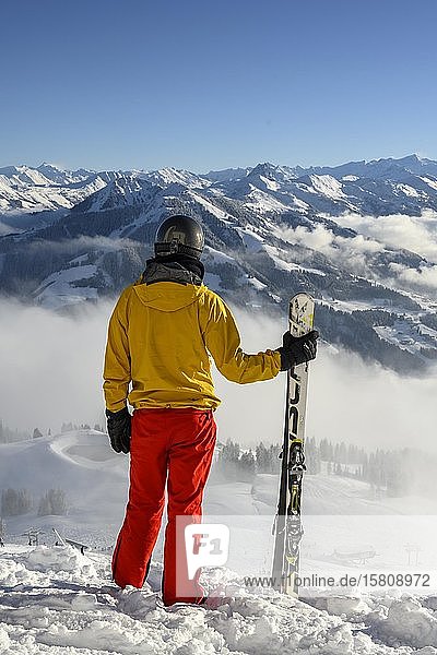 Skier standing at the ski slope holding ski  view into the distance  snowy mountain panorama  summit Hohe Salve  SkiWelt Wilder Kaiser Brixenthal  Hochbrixen  Tyrol  Austria  Europe