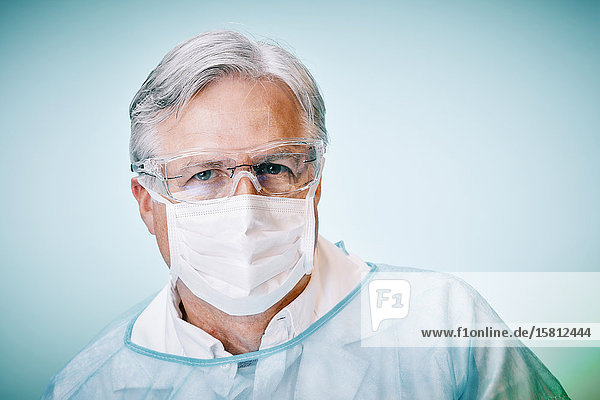 Arzt mit Schutzbrille und Mundschutz blickt in Kamera