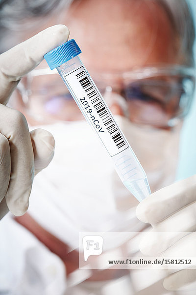 Älterer Laborant hält Reagenzglas mit Coronavirus Probe in Kamera
