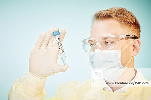 Junger Laborant blickt auf Reagenzglas mit Cornoravirus Probe