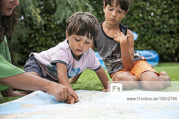 Frau und zwei Jungen sitzen im Freien auf einer Wiese und schauen auf eine Weltkarte.