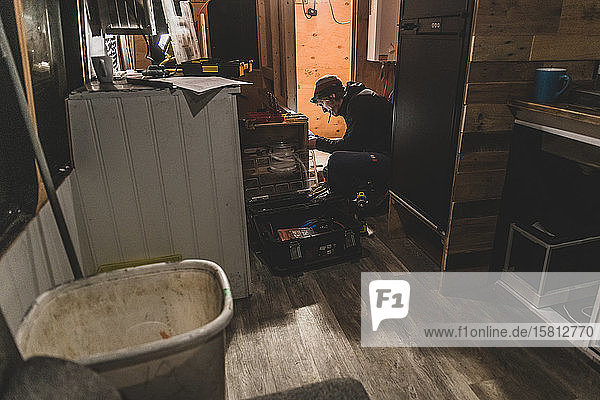 Mann mit Werkzeugkasten kniend in einer Küche  beim Heimwerken.