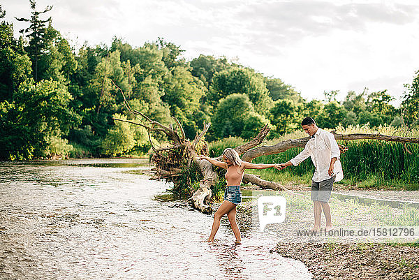 Junges Paar  das Hand in Hand an einem Flussufer geht.
