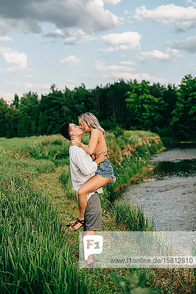 Junges Paar steht auf einem Weg an einem Fluss  umarmt und küsst sich.