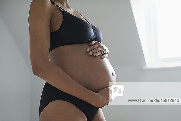 Schwangere Frau in BH und Höschen hält Bauch