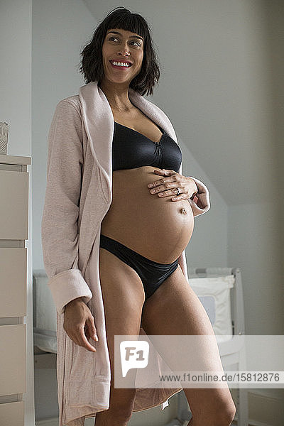 Glückliche schwangere Frau in BH und Höschen hält Bauch