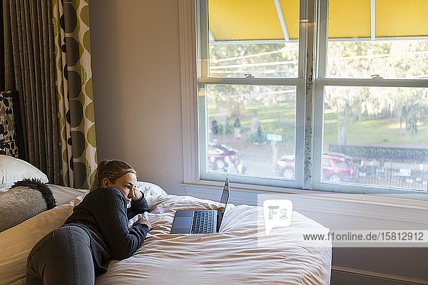 Eine dreizehnjährige Teenagerin liegt im Bett und schaut auf ihren Laptop