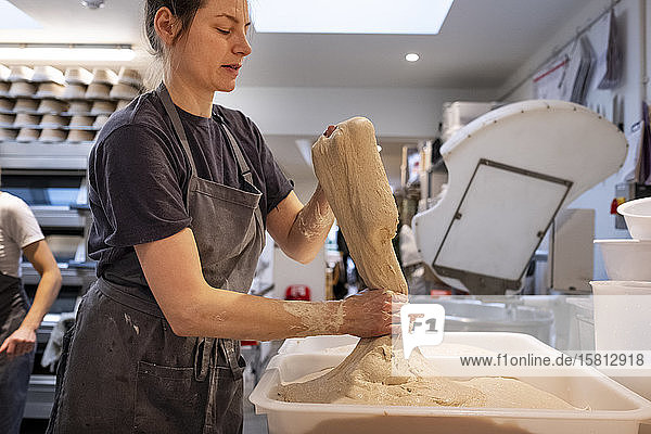 Frau mit Schürze  die in einer handwerklichen Bäckerei steht und mit Sauerteig arbeitet.