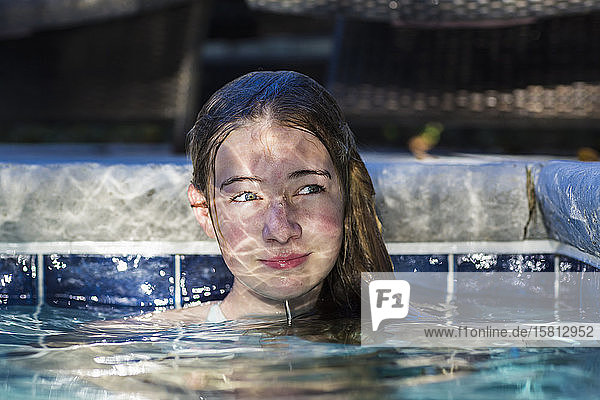 Ein dreizehnjähriges Teenagermädchen in einem Schwimmbad mit reflektiertem Licht  das auf ihrem Gesicht spielt