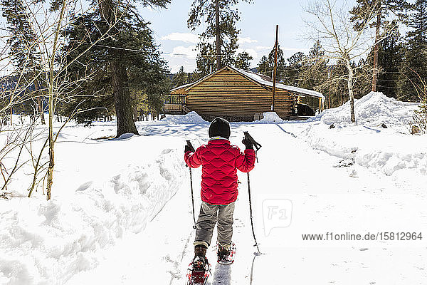 Rear view of young boy in a red jacket snow shoeing