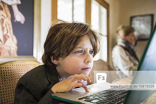 Ein sechsjähriger Junge  der zu Hause auf einem Laptop mit dem Cursor-Touchpad tippt.