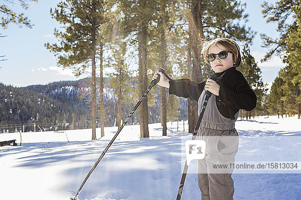 A six year old boy in woodland holding ski poles