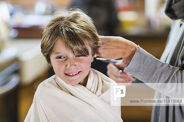 A six year old boy getting his hair cut at home by his mother