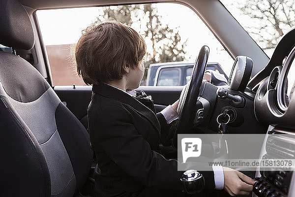 Ein sechsjähriger Junge sitzt im Auto und hält ein Lenkrad