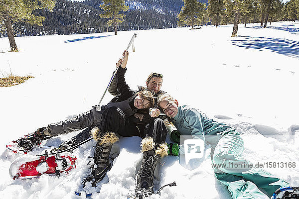 Eine Frau und ihre zwei Kinder  ein Mädchen im Teenageralter und ein Junge  die in Schneeschuhen und Skiausrüstung im Schnee liegen.
