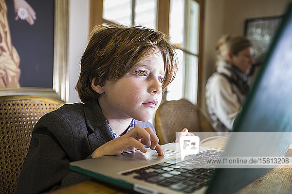 Ein sechsjähriger Junge tippt zu Hause auf einem Laptop