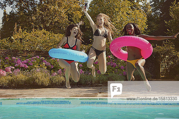 Verspielte Teenager-Freundinnen  die in den sonnigen Sommer-Swimmingpool springen