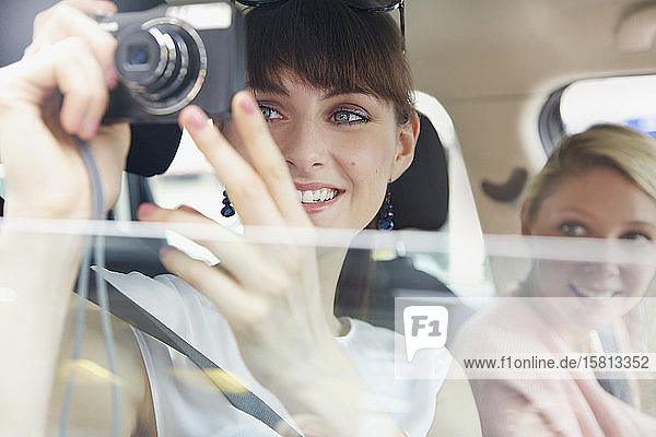 Glückliche junge Frau  die vom Autofenster aus eine Digitalkamera benutzt