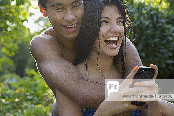 Glückliches  zärtliches junges Paar  das auf einer Sommerterrasse sein Smartphone benutzt