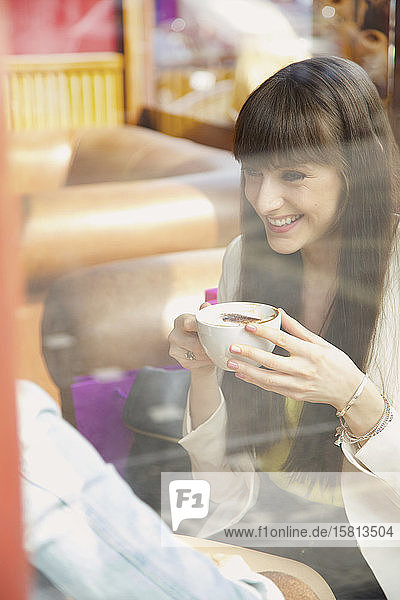 Glückliche junge Frau genießt einen Cappuccino im Caféfenster