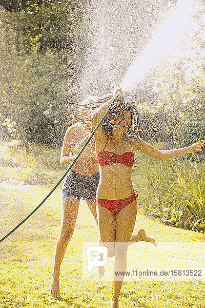 Verspielte junge Frau im Bikini sprüht Wasser mit Schlauch im Sommer Hinterhof