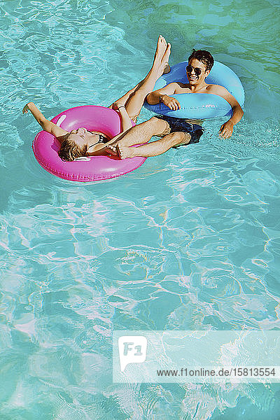 Glückliches junges Paar mit aufblasbaren Ringen im sonnigen Sommerschwimmbad