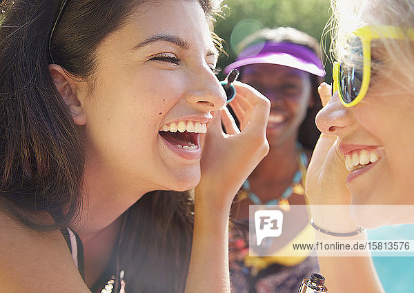 Glückliche Teenager-Freundinnen tragen auf einer sonnigen Terrasse Wimperntusche auf