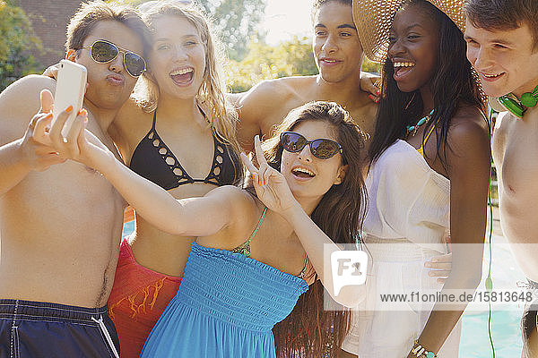 Happy teenage friends taking selfie with smart phone on sunny summer patio