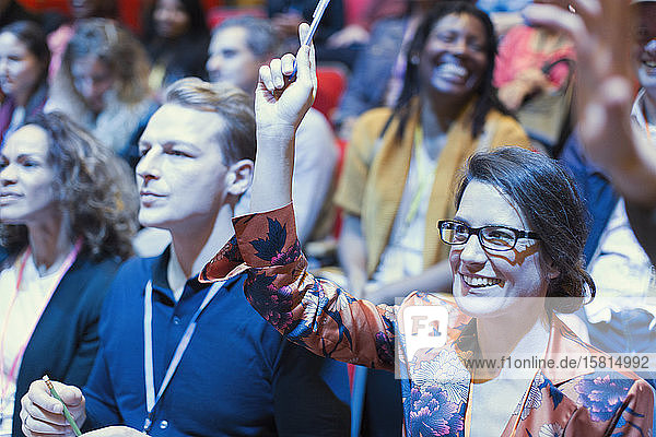 Lächelnde Frau im Konferenzpublikum hebt die Hand