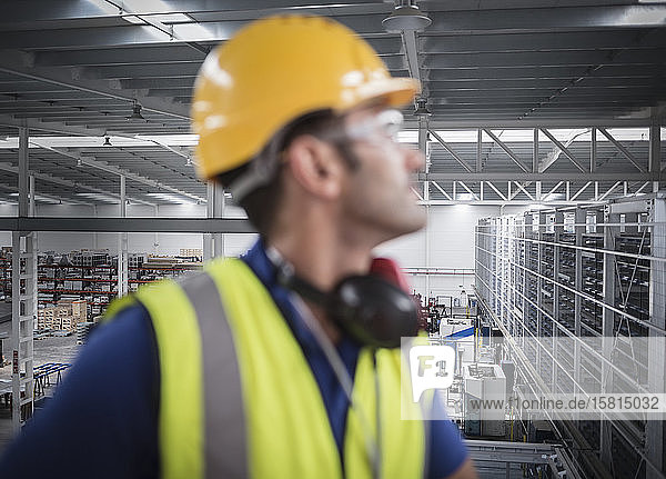 Männlicher Arbeiter  der auf einer Plattform in einer Fabrik wegschaut