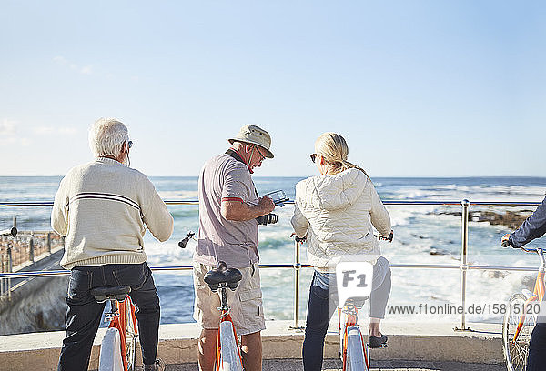 Active senior tourists on bicycles looking at sunny ocean view