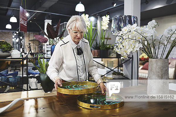 Ältere Frau betrachtet Tabletts in einem Geschäft für Wohnkultur