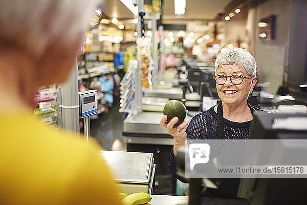 Lächelnde ältere weibliche Kassiererin  die einem Kunden an der Kasse eines Lebensmittelgeschäfts hilft