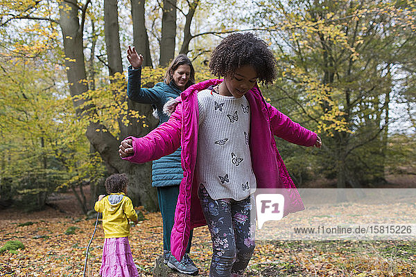 Mutter und Töchter balancieren auf einem umgestürzten Baumstamm im Herbstwald