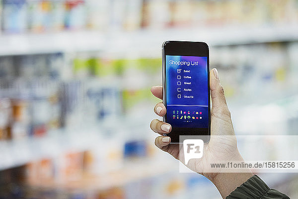 Persönliche Perspektive einer Frau  die im Supermarkt die digitale Einkaufsliste auf ihrem Smartphone überprüft