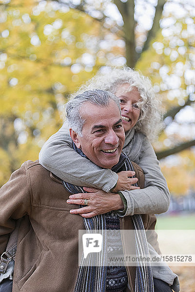 Verspieltes  lächelndes älteres Paar nimmt im Herbst im Park Huckepack