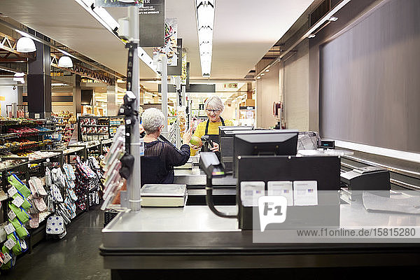Senior female cashier helping customer at supermarket checkout