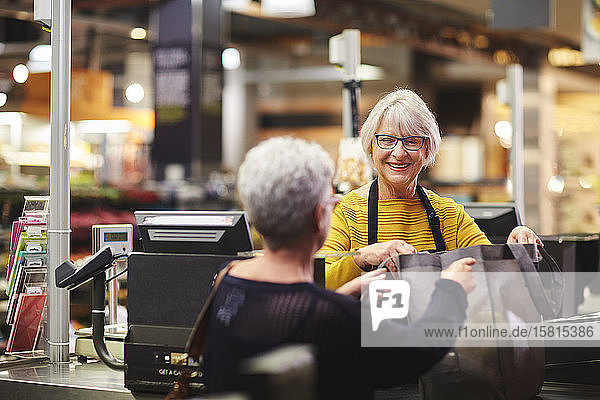 Friendly senior female cashier helping customer supermarket checkout