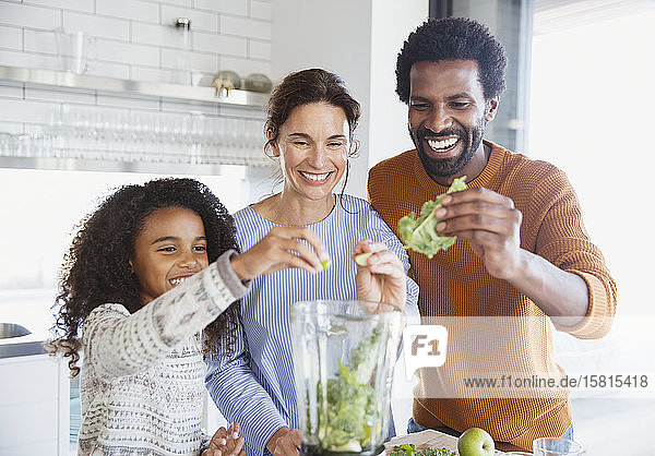 Lächelnde multiethnische Familie bei der Zubereitung eines grünen Smoothies im Mixer in der Küche