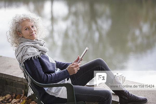 Porträt einer selbstbewussten  aktiven älteren Frau  die ein digitales Tablet am Parkteich benutzt