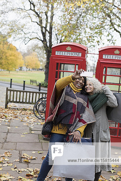 Ältere Frauen Freunde mit Einkaufstaschen nehmen Selfie im Herbst Park vor roten Telefonzellen