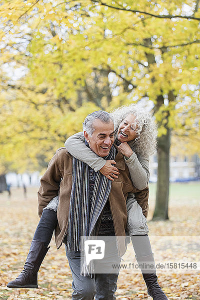 Verspieltes älteres Paar nimmt im Herbst Huckepack im Park